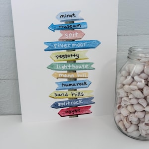 May include: A watercolor painting of a wooden signpost with multiple arrows pointing in different directions. Each arrow has a different color and features a handwritten word, including "minot", "museum", "Spit", "river moor", "Peggotty", "lighthouse", "mann hill", "humarock", "Sand hills", "split rock", and "egypt".