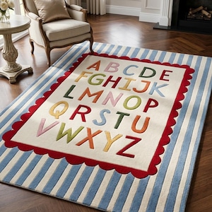 May include: A rectangular area rug featuring a cream-colored center with the alphabet in multi-colored letters. The center is bordered by a red scalloped edge, surrounded by a blue and white striped pattern covering the rest of the rug surface.