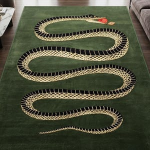 May include: A rectangular area rug in a deep forest green colour featuring a large, winding snake graphic. The snake has a cream-coloured underbelly with black scales and holds a small red apple with a brown leaf in its mouth.