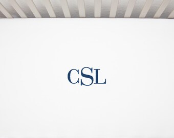 Può includere: Lenzuolo per culla bianco con monogramma "CSL" ricamato in blu navy al centro.