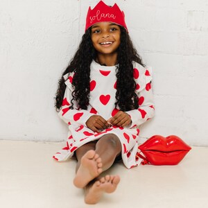 little girl wearing a red crown with her name embroidered on it