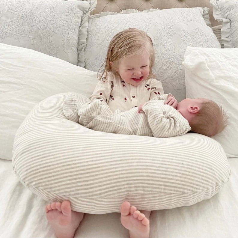 new sister holding newborn baby brother with a nursing pillow