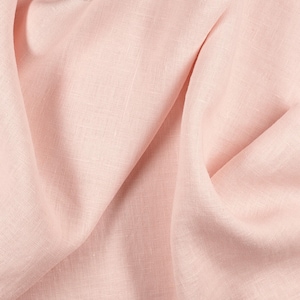 May include: A close-up of a soft, pale pink linen fabric with a textured weave. The fabric is folded and draped, showing its natural wrinkles and folds.