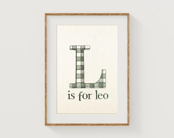 May include: Framed print featuring the letter "L" in a green and white gingham pattern. The text "is for leo" is below the letter. The artwork is set against a cream-colored background and framed in a light brown wooden frame.