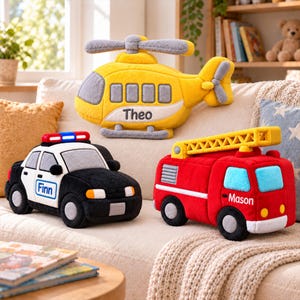 May include: Three plush vehicle toys including a yellow helicopter with the name Theo, a black and white police car with the name Finn, and a red fire truck with the name Mason. Each soft toy features embroidered details and wheels.