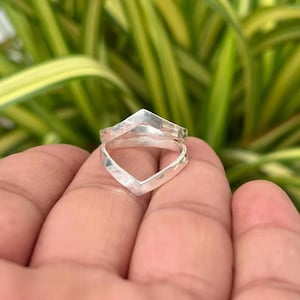May include: A silver ring featuring a double chevron design with a hammered, textured finish. The band consists of two V-shaped components joined together, creating a geometric silhouette with a polished, reflective metallic surface.