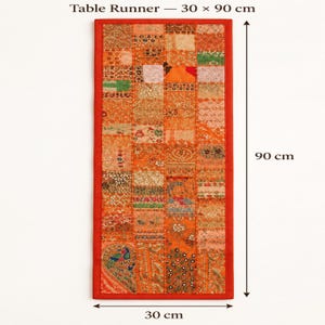May include: A rectangular table runner featuring a patchwork design of orange fabric squares with intricate embroidery, sequins, and mirror work. The runner measures 30 by 90 cm and includes a peacock motif in the bottom left corner with a red border.