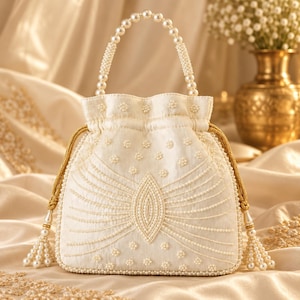 May include: An off-white drawstring handbag featuring an intricate pattern of small white beads and pearls. The bag includes a pearl-beaded handle, gold-toned braided drawstrings with beaded tassels, and a central almond-shaped beaded design.