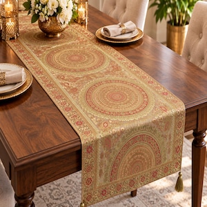 Puede incluir: Un camino de mesa rectangular largo con un patrón repetitivo de grandes medallones circulares en tonos oro, cobre y rojo intenso. La tela tiene una textura tejida intrincada con bordes florales ornamentados y una borla decorativa al final.