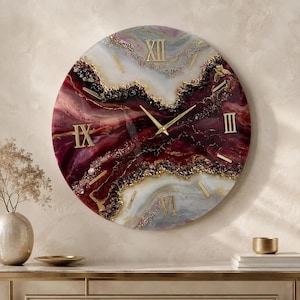 Può includere: Un orologio da parete rotondo con un design in resina vorticoso nei toni del bordeaux intenso, bianco e grigio. Il quadrante presenta numeri romani dorati alle posizioni delle dodici, tre, sei e nove, con lancette dorate e accenti in oro.