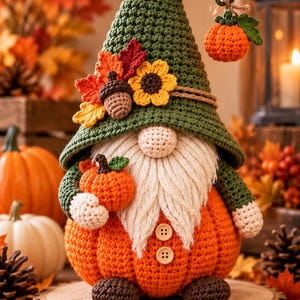 May include: A crochet gnome figurine featuring a tall green hat adorned with fabric leaves, a sunflower, and an acorn. The gnome has a white yarn beard, a round nose, and a pumpkin-shaped body with two buttons, holding a small orange pumpkin.