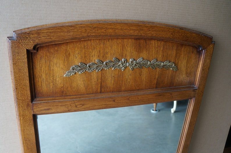 Może przedstawiać: Lustro w drewnianej ramie z wzorem z liści złota. Lustro ma fazowane krawędzie i prosty, elegancki design.