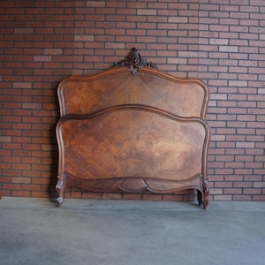 May include: A vintage wooden bed frame with a curved headboard and footboard. The frame is made of dark wood with a detailed grain pattern. The headboard features ornate carvings at the top, adding a touch of elegance to the bedroom furniture.