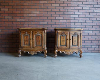 May include: A pair of wooden nightstands featuring two doors each with carved shell motifs at the top and bottom, dark wood finish, and intricate painted floral details on the door panels, supported by four curved legs with decorative feet.