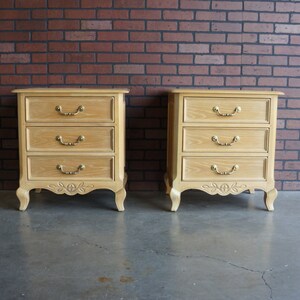 May include: Two wooden nightstands with three drawers each. The nightstands have ornate carvings and gold-colored hardware.