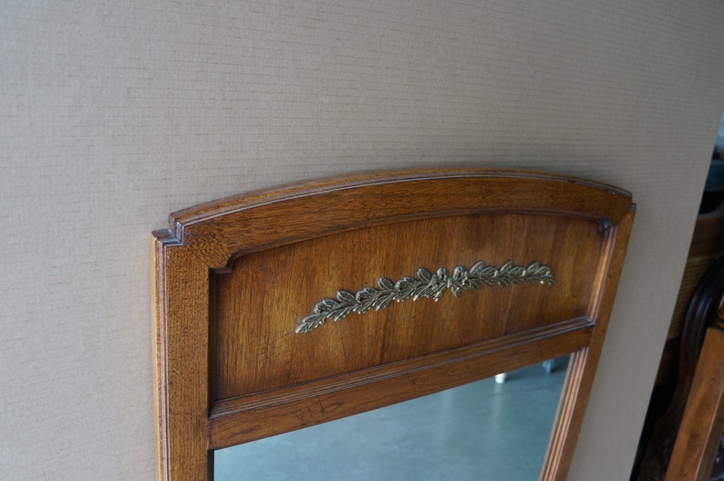 Może przedstawiać: Lustro w drewnianej ramie z ozdobnym wzorem z liści z mosiądzu. Lustro ma fazowane krawędzie i prosty, elegancki design.
