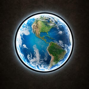 Op de afbeelding: Een ronde wandlamp met een satellietfoto van de aarde in hoge resolutie, waarop Noord- en Zuid-Amerika te zien zijn met blauwe oceanen, groene landmassa's en witte wolkenformaties, omringd door een dunne zwarte rand met een helder witte gloed.