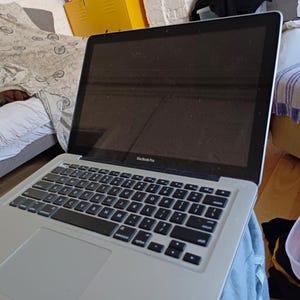 Puede incluir: Un ordenador portátil MacBook Pro plateado con teclado negro y marco de pantalla negro. La pantalla está oscura y muestra el texto MacBook Pro en la parte inferior central. El dispositivo cuenta con un chasis de metal plateado, un trackpad y teclado.