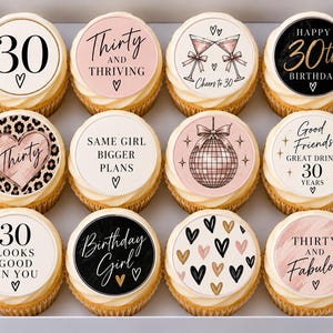 以下が含まれることがあります： 箱に入った12個のカップケーキのセット。それぞれに、数字の30、Thirty and ThrivingやBirthday Girlといったテキスト、ハート、ミラーボール、マティーニグラスなどのグラフィックが描かれた円形の食用トッパーが飾られています。