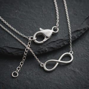 Op de afbeelding: Een sterling zilveren ketting met een hanger in de vorm van een oneindigheidssymbool en een karabijnsluiting. De sluiting is duidelijk gestempeld met het getal 925, wat de zuiverheid van het metaal aangeeft. De ketting heeft een verlengstuk.