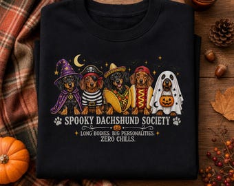 May include: A black sweatshirt featuring five dachshunds in Halloween costumes: a wizard, a pirate, a taco, a hot dog, and a ghost. The text reads: SPOOKY DACHSHUND SOCIETY, LONG BODIES. BIG PERSONALITIES. ZERO CHILLS. The design includes stars and bats.