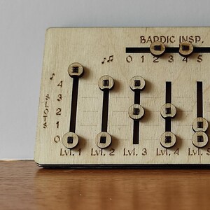 Op de afbeelding: Een rechthoekig spelbord van lichtgekleurd hout met in laser gegraveerde tekst en schuifregelaars. Het bord bevat labels voor Bardic Insp., Concentration en spell slots van Lvl. 1 tot Lvl. 9, voorzien van muzieknoot-iconen en schalen.