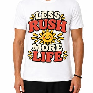 Op de afbeelding: Een wit T-shirt met korte mouwen en een grafische print met de tekst "LESS RUSH MORE LIFE" in dikke rode en zwarte letters. Een geel lachend zonicoon is geplaatst tussen de woorden "RUSH" en "MORE" op de voorzijde van het T-shirt.