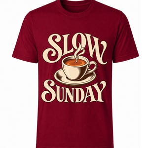 Könnte beinhalten: Ein bordeauxrotes Kurzarm-T-Shirt mit einer Grafik einer Kaffeetasse auf einer Untertasse, aus der Dampf aufsteigt. Der Text SLOW ist in einer cremefarbenen, stilisierten Schrift über der Tasse und der Text SUNDAY unter der Tasse gedruckt.