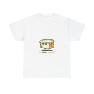 May include: A white short-sleeve t-shirt featuring a central graphic of a white container wearing sunglasses and a tan trench coat. Below the graphic, the text reads, "I was [redacted] at that potluck." The design is centered on the chest area.
