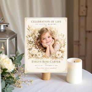 May include: A rectangular memorial sign featuring the text CELEBRATION OF LIFE, IN LOVING MEMORY, EVELYN ROSE CARTER, MAY 18, 2017 - SEPTEMBER 22, 2023, and Forever loved, forever remembered, with a portrait of a young child surrounded by white flowers.