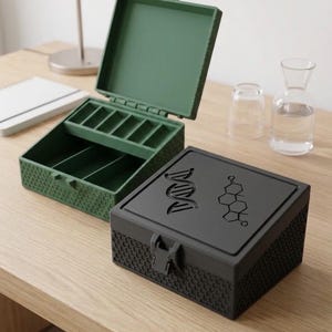 Könnte beinhalten: Zwei quadratische Aufbewahrungsboxen mit einem strukturierten Wabenmuster an den Seiten. Eine Box ist dunkelgrün und geöffnet, mit sichtbaren Innenfächern. Die andere Box ist schwarz, geschlossen und zeigt eine DNA-Helix und Strukturformel.