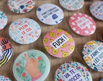 Peut inclure: Un ensemble de badges ronds avec des motifs variés, incluant des fleurs, des visages souriants faisant des doigts d'honneur, et des textes comme FUCK, PLEIN LE CUL, et VA TE PONCER LA BITE.