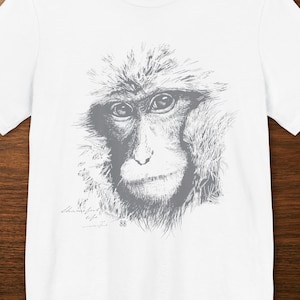 May include: A white short-sleeved t-shirt featuring a detailed gray sketch of a monkey's face centered on the chest. Below the monkey illustration, there is small, cursive script text that reads "thankful to be wonderful" followed by the number 88.