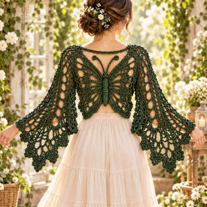 May include: A dark green crochet top featuring a large butterfly design on the back with intricate openwork patterns and wide, flared sleeves. The garment is paired with a long, light-coloured, tiered skirt, creating a layered look with detailed stitching.