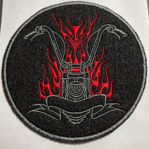 May include: Black and red embroidered patch with a motorcycle engine design, flames, and a banner. The patch is circular and has a gray border.