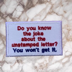 May include: Embroidered patch with the text "Do you know the joke about the unstamped letter? You won't get it." The text is in red and blue on a light blue background, with a purple border.