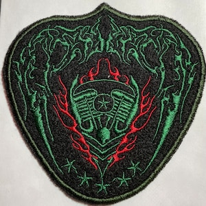 May include: Green and red embroidered patch with a stylized engine design, flames, and a star. The patch is shaped like a shield and has a black background.