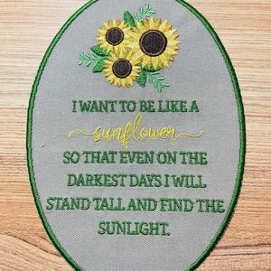 May include: A green oval-shaped patch with a white background and green stitching around the edges. The patch features an embroidered image of three yellow sunflowers with brown centers and green leaves. The text "I WANT TO BE LIKE A sunflower SO THAT EVEN ON THE DARKEST DAYS I WILL STAND TALL AND FIND THE SUNLIGHT." is embroidered in yellow on the patch.