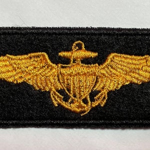 May include: A gold embroidered patch with a winged anchor on a black background. The patch is rectangular and has a stitched border.