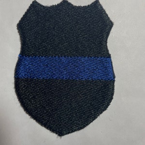 May include: Black and blue embroidered patch in the shape of a police badge with a thin blue line.