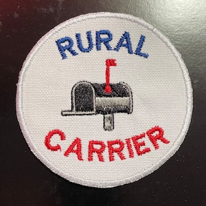 May include: A round white patch with the words "RURAL CARRIER" embroidered in blue and red. A black and gray mailbox with a red flag is in the center.