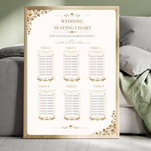Puede incluir: Un cartel de plano de asientos de boda en un marco de madera clara con papel color crema, texto dorado y detalles florales. El texto dice Wedding Seating Chart, Find Your Seat & Celebrate With Us, y enumera seis mesas con espacios para nombres.