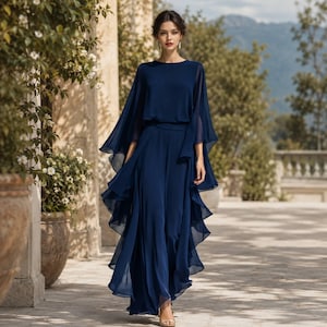 May include: A floor-length navy blue jumpsuit featuring a round neckline, a fitted waist, and wide, flowing cape-style sleeves. The garment includes layered, ruffled fabric panels that cascade down the legs, creating a voluminous silhouette.