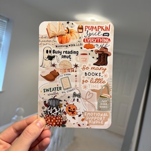 May include: A rectangular sticker sheet featuring a collage of autumn-themed illustrations and text, including a pumpkin, a ghost reading a book, brown boots, a stack of pumpkins, and phrases like Pumpkin Spice and Everything Nice and Busy reading smut.