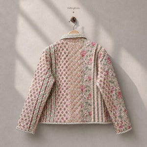May include: A quilted jacket featuring a patchwork design with various floral patterns in shades of pink, green, and beige. The garment has a collared neckline, long sleeves, and striped trim along the edges. The text GiftingEdits is visible.