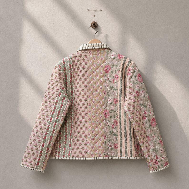 May include: A quilted jacket featuring a patchwork design with various floral patterns in shades of pink, green, and beige. The garment has a collared neckline, long sleeves, and striped trim along the edges. The text GiftingEdits is visible.