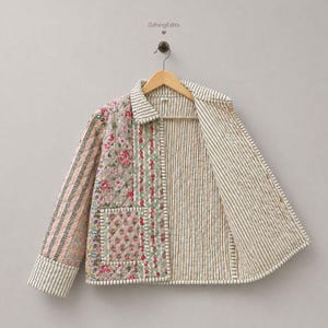 May include: A quilted jacket featuring a patchwork design with floral patterns in pink, green, and beige, contrasted by black and white vertical stripes on the sleeves, collar, and interior lining. The jacket includes a front pocket and button closure.