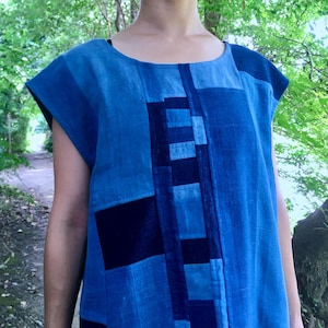 May include: A short-sleeved top featuring a patchwork design of various blue shades, including navy and light blue. The garment has a round neckline and a straight hem, constructed from rectangular fabric panels of differing blue tones.