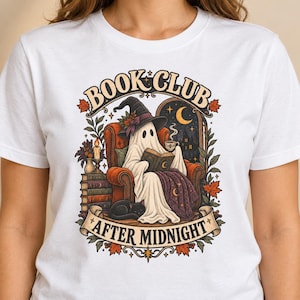 May include: A white t-shirt featuring a graphic of a ghost wearing a witch hat, sitting in an armchair, reading a book, and holding a cup. A black cat sleeps nearby. The text reads "BOOK CLUB" at the top and "AFTER MIDNIGHT" at the bottom.