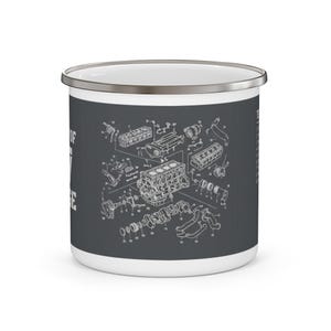 Pode incluir: Uma caneca de esmalte cinza-escuro com uma borda prateada, apresentando um desenho técnico de linhas brancas de um diagrama de motor explodido com peças numeradas. O design é impresso na lateral da caneca, que tem uma forma cilíndrica lisa.